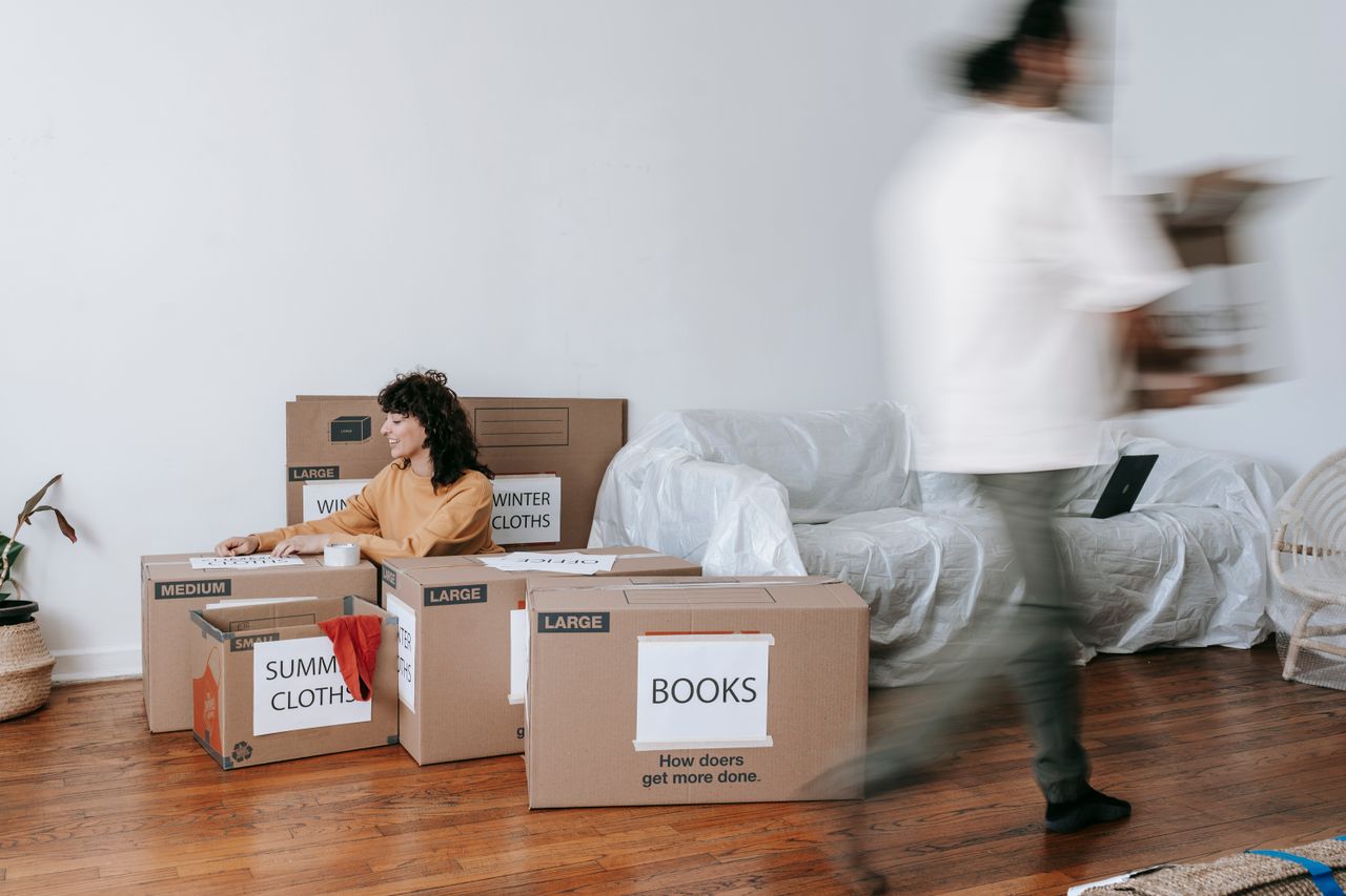 who-we-are A couple packing labeled boxes in a minimalist living room, preparing for moving day.