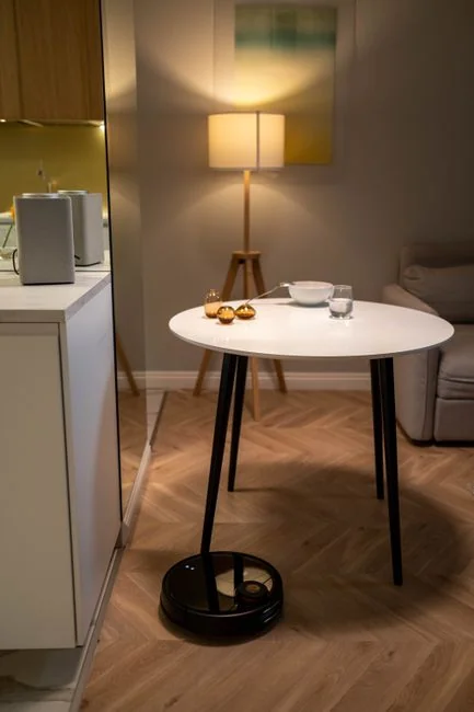 services-04 Une personne soulève un canapé dans un salon minimaliste avec un parquet en bois.